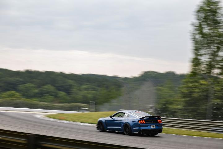 blue mustang racing around a curved track on an overcast day